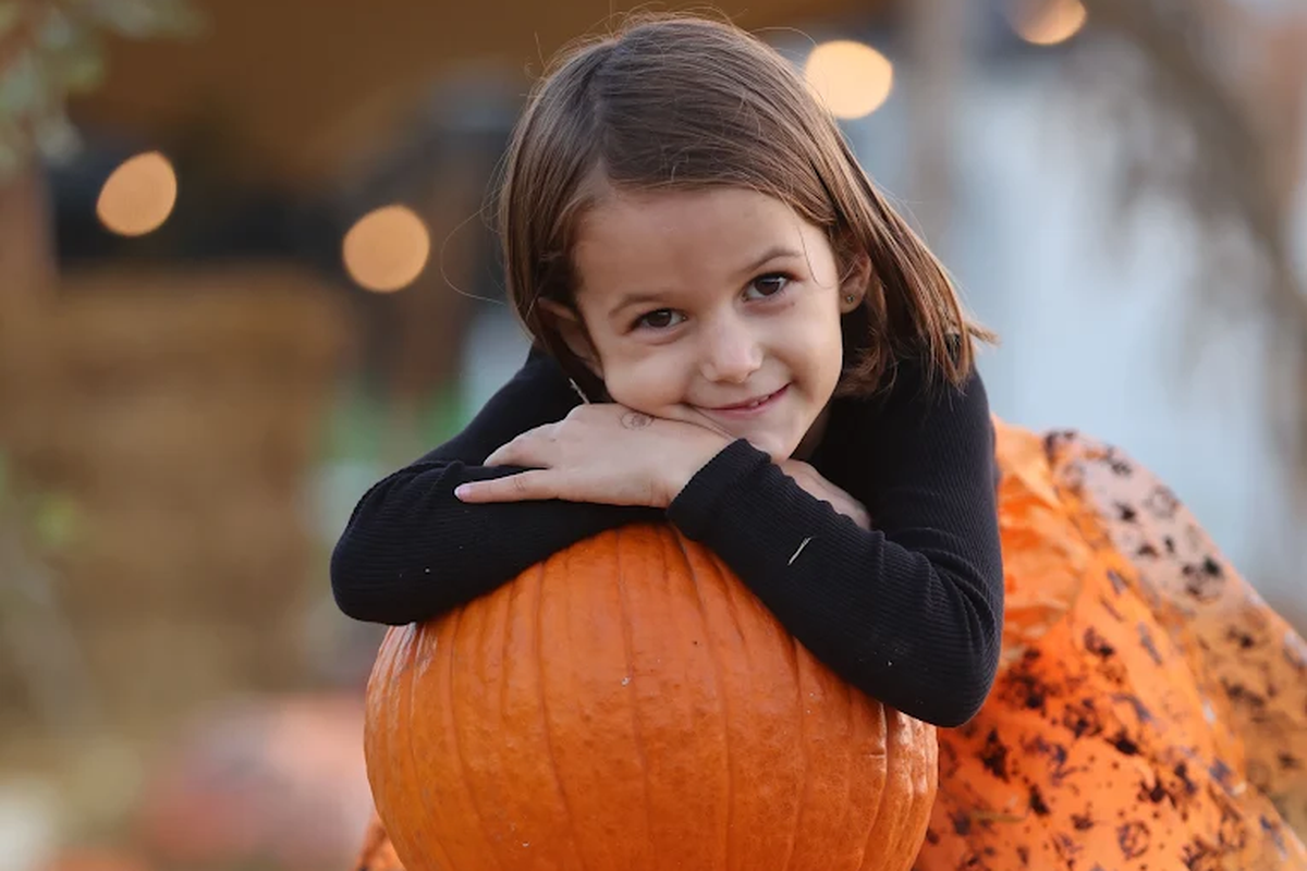 Smiling girl leaning on a pumpkin for Halloween